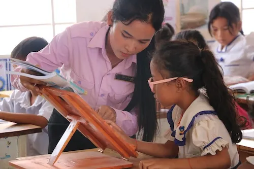 A teacher is explaining something to one of her students. The student is a girl wearing glasses.