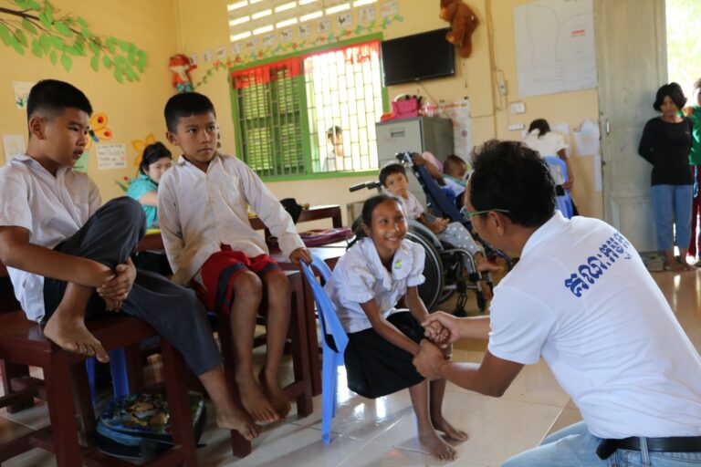In a classroom, a man gently holding a little girl's hands.