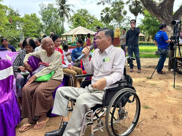 a man with disabilities sitting on a wheelchair speaking through a microphone.