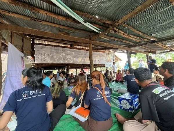 Group of people from behind, they are seated and are listening to someone speaking.