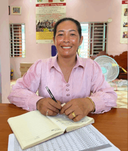 Ms. Thai Soda is looking at the camera smiling, she has a notebook in front of her. She is sitted inside.