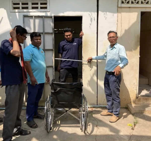 Multiple men next to a door. One is holding a tape measure to show the door is too narrow and not accessible.