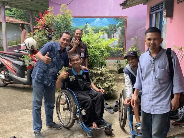 Group of men smiling at the camera, two are seated in wheelchairs.