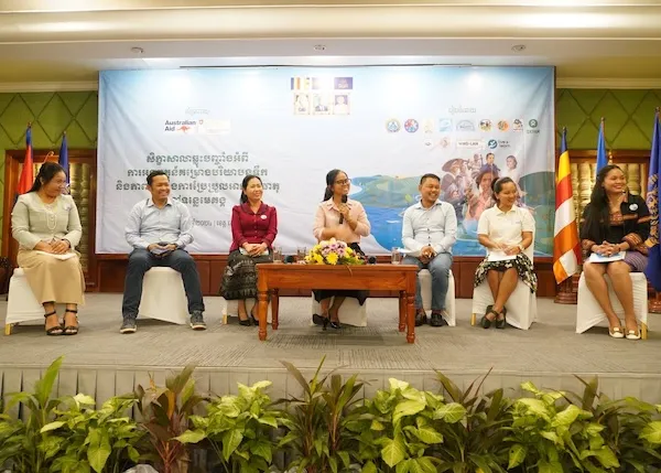 People seated on a stage, one woman is speaking with a microphone.