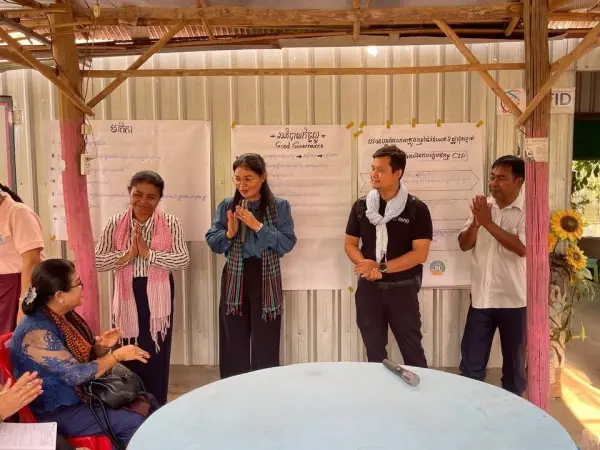 four standing people saluting a sitting woman.