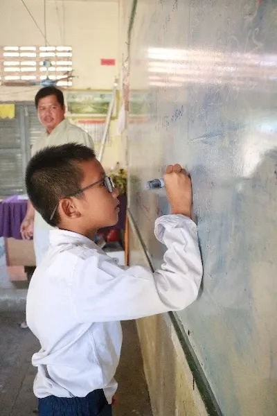 Mr. Leng Bunchhay is writing on a white board in a classroom.
