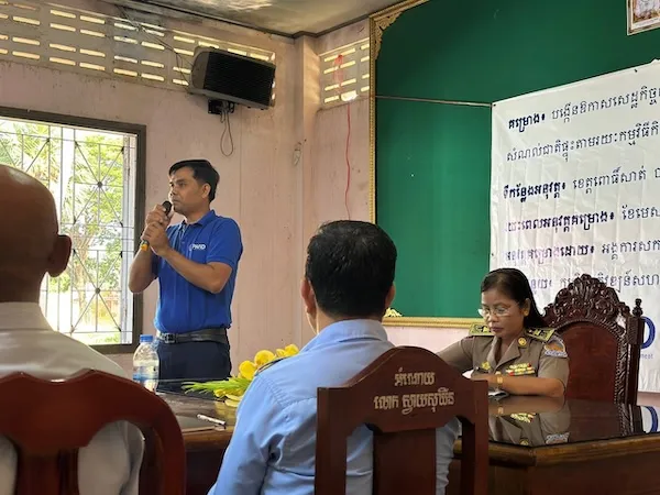 One PAfID member standing up and speaking in front of multiple people in a room.