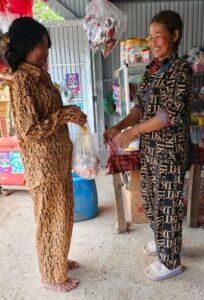 Ms. Vouen Saem is handing an bag to a customer in her shop.