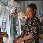 Ms Vouen Saem is handing a bag to a customer in her shop. She is smiling.