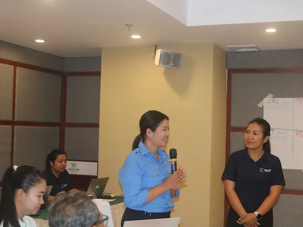 Woman standing up and speaking with a microphone.