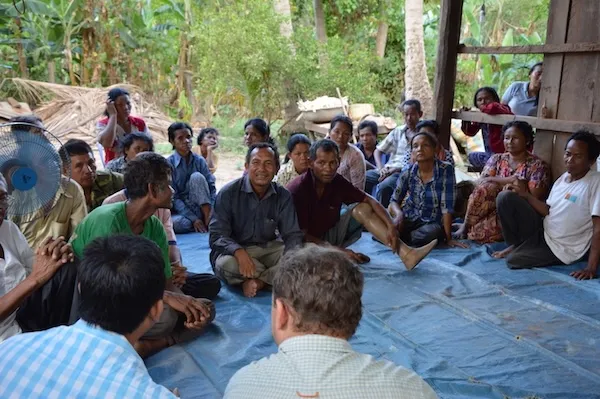 A group of people seated on the floor during a village meeting.