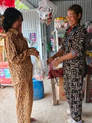 Ms Vouen Saem is handing a bag to a customer in her shop. She is smiling.
