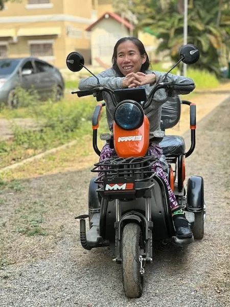 Woman with disability seating on a motorbike adapted to her.She is outside and smiling.