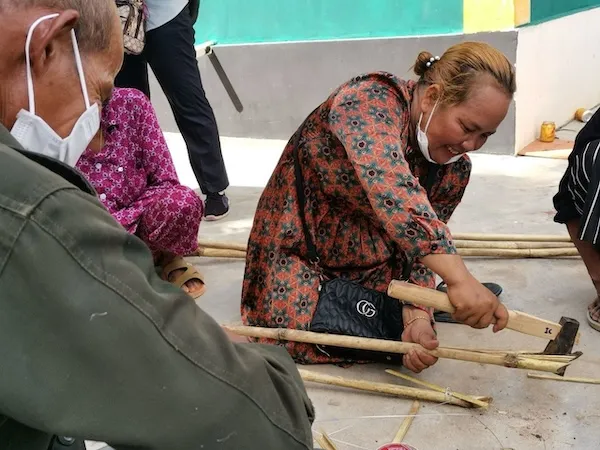a woman smiling, sitting on the ground and splitting bamboo.